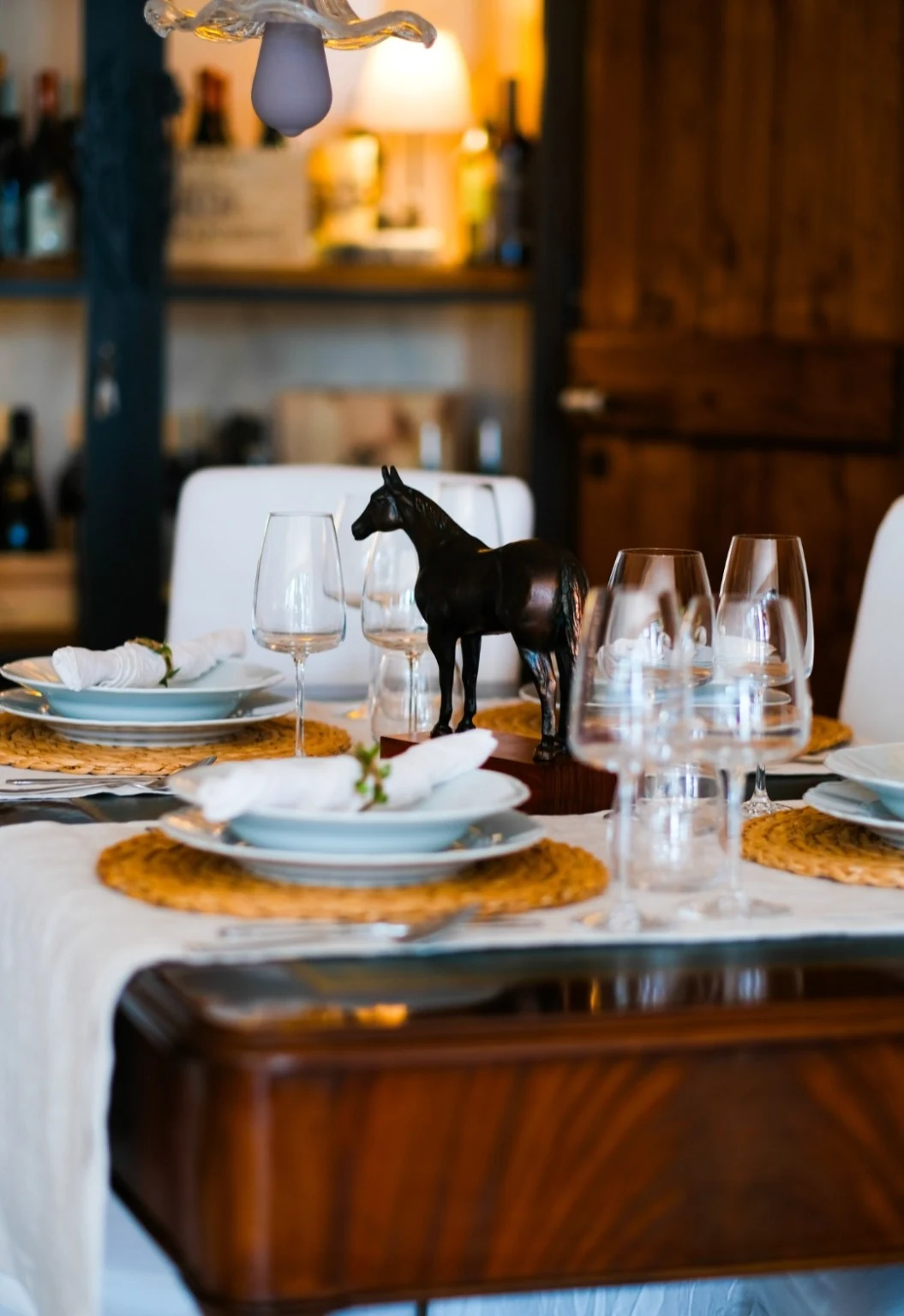 Tavola apparecchiata con porcellane, calici e scultura di cavallo nero